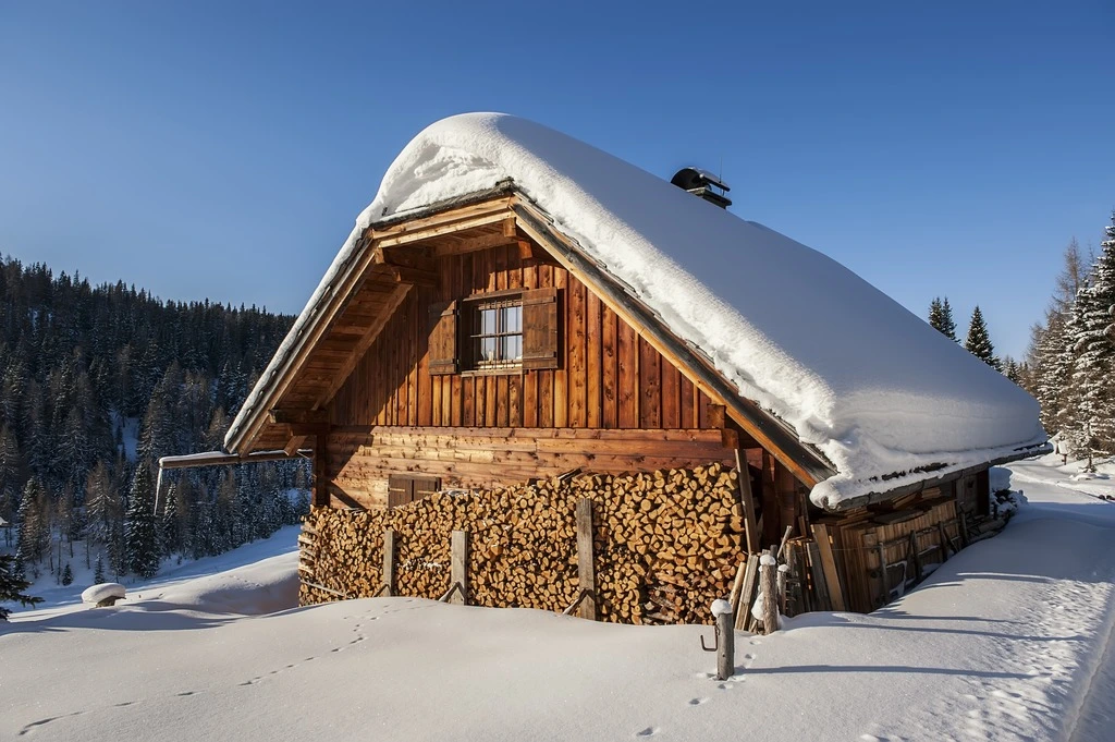 Kleines Chalet aus Holz tief verschneit im sonnigen Winter in Österreich