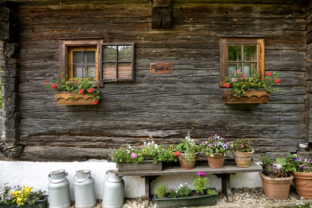 Altes Bauernhaus als Hütte in Österreich mit Blumen und Milchkannen davor